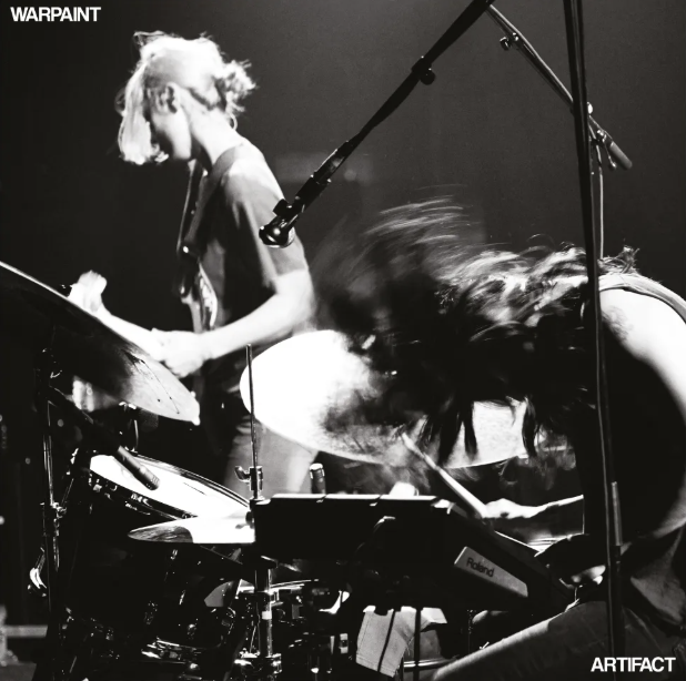 Album cover artwork for Warpaint's 'Artifact' featuring a black and white image of a band performing live on stage.
